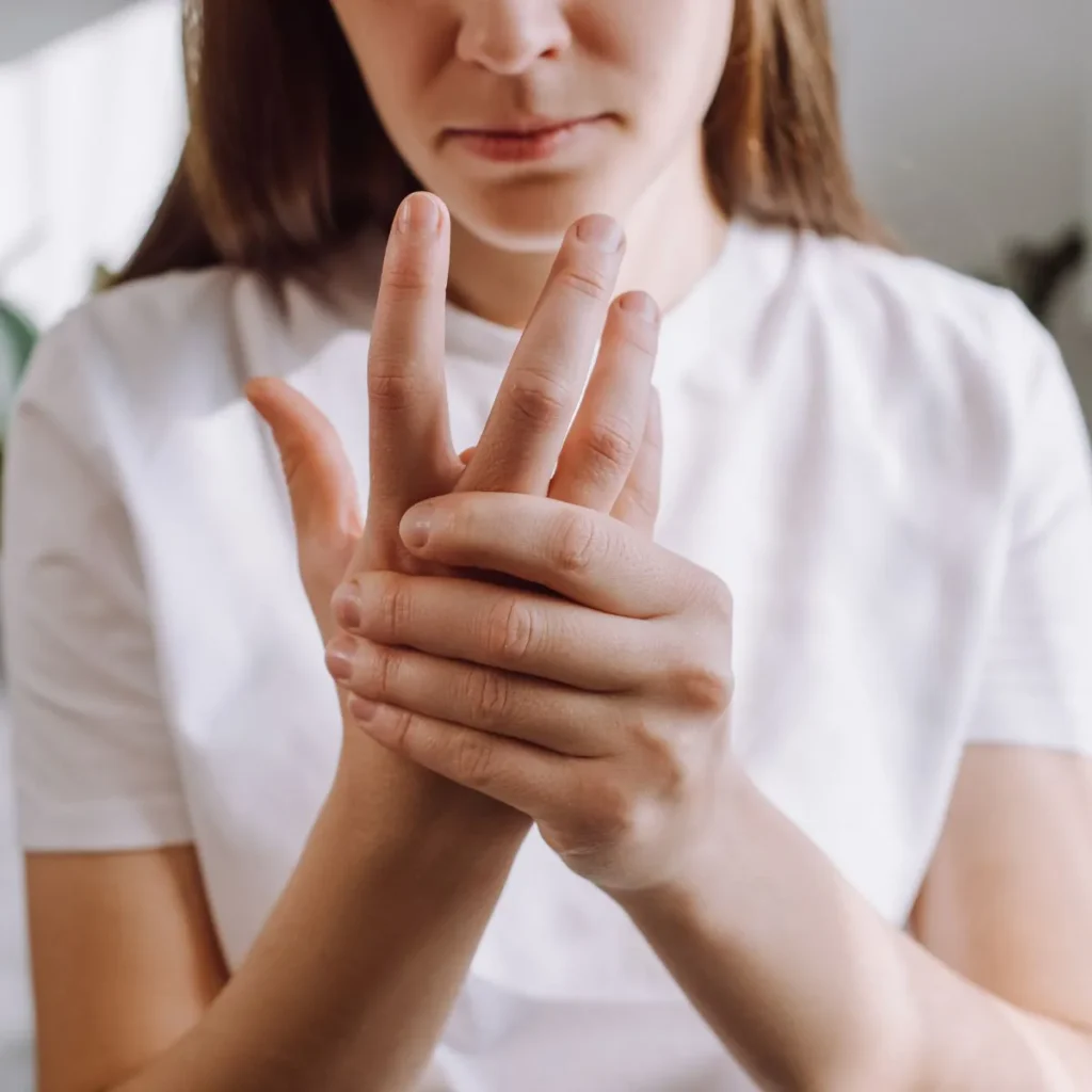 A person in a white shirt is holding and massaging their left hand, appearing to experience discomfort or pain in their fingers.